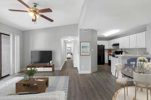 A modern living room with a television, a dining table set for four, and a kitchen area in the background.